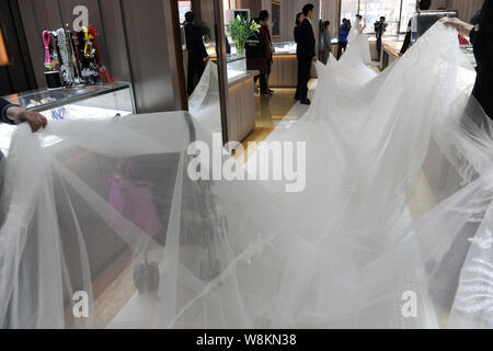 Un modello che indossa un abito nuziale con un 101-metro-long tail trasportati dai membri del personale di un abito da sposa azienda pone per le foto e i video in un negozio Foto Stock