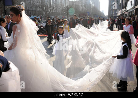 Un modello che indossa un abito nuziale con un 101-metro-long tail portati dai ragazzi e i membri del personale di un abito da sposa azienda sfilate lungo una via d Foto Stock