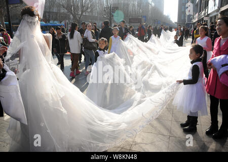 Un modello che indossa un abito nuziale con un 101-metro-long tail portati dai ragazzi e i membri del personale di un abito da sposa azienda sfilate lungo una via d Foto Stock