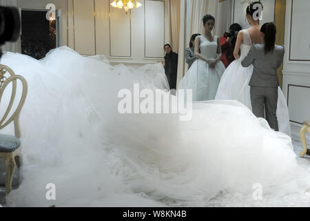 Un membro del personale di un abito da sposa azienda aiuta un modello che indossa un abito nuziale con un 101-metro-long tail serrare il vestito in un negozio della società Foto Stock