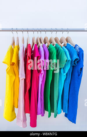 Moda Abbigliamento su rack - luminoso stand colorati di rainbow selezione di t-shirt. Scelta della femmina alla moda di usura sulle staffe in negozio un armadio o pulizie di primavera concetto. Estate Home guardaroba. Foto Stock