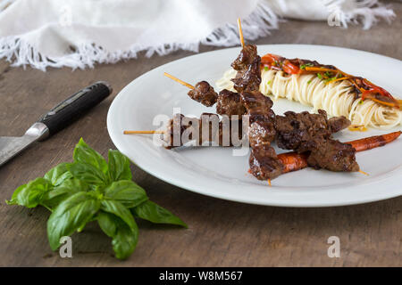 Stile asiatico grigliate di teriyaki spiedini di carne su una piastra bianca, vista dall'alto. Delizioso antipasto Foto Stock