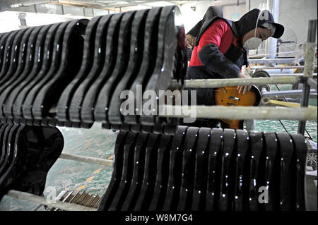 --FILE--un lavoratore cinese lucidi di una chitarra elettrica in corrispondenza di una fabbrica di strumenti musicali nella città di Huainan, est cinese della provincia di Anhui, 1 dicembre 2015. Foto Stock