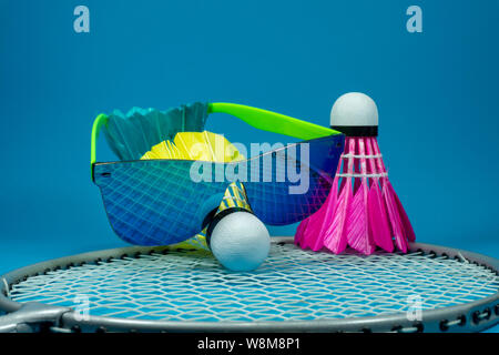 Selvaggina di penna colorati badminton volano con occhiali da sole in appoggio su una racchetta su uno sfondo blu in una chiusura ancora vita Foto Stock