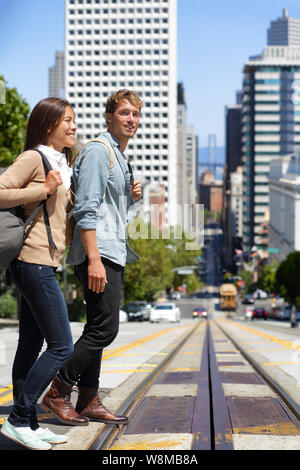 La città di San Francisco lo stile di vita delle persone. Giovani interracial giovane gli studenti a camminare su una strada di città incrocio stradale attraverso cavo ferroviaria sistema auto. Destinazione famosa per i turisti che visitano la città urban center. Foto Stock