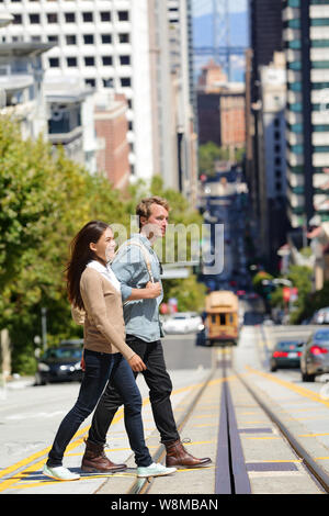 La città di San Francisco lo stile di vita delle persone. Giovani interracial giovane gli studenti a camminare su una strada di città incrocio stradale attraverso cavo ferroviaria sistema auto. Destinazione famosa per i turisti che visitano la città urban center. Foto Stock