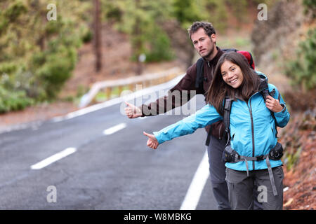 Gli escursionisti di viaggio giovane che mostra i pollici fino sulla strada per fare l'autostop durante il viaggio. Felice giovani interracial backpackers hitchhikers in attesa per un rideshare, la condivisione di una corsa in vacanza vacanze. Foto Stock