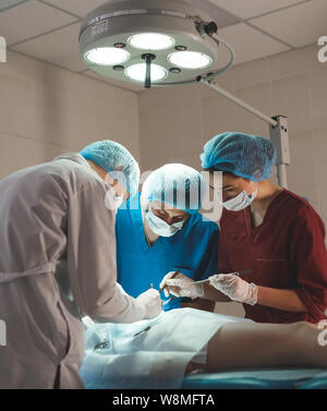 Gruppo di chirurghi al lavoro che operano in sala operatoria. Medicina di rianimazione team indossando maschere di protezione tenendo in acciaio strumenti medici Foto Stock