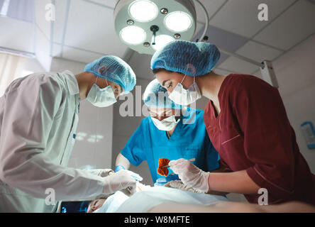 Gruppo di chirurghi al lavoro che operano in sala operatoria. Medicina di rianimazione team indossando maschere di protezione tenendo in acciaio strumenti medici Foto Stock