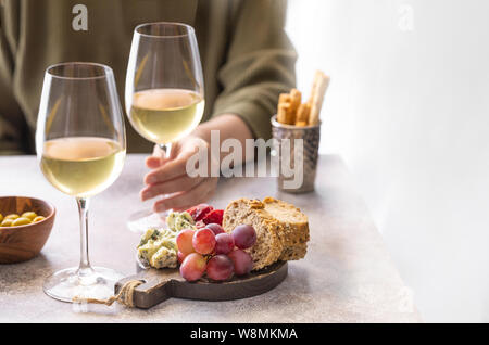 Donna che mantiene un bicchiere di vino bianco nel ristorante. Diversi spuntini, blu di formaggio, olive, baguette fette e salumi. Degustazione lifestylebac party Foto Stock