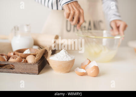 Giovane di mani sbattere le uova con lo zucchero per cuocere la torta di frutta. Maschio di cucinare la pasta per la torta sul tavolo bianco Foto Stock