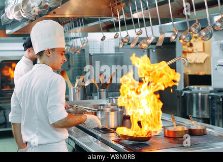 Cucina moderna. I cuochi preparano pasti sul fornello nella cucina del ristorante o albergo. Il fuoco in cucina. Foto Stock