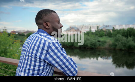 Giovani afro american guy a camminare nel parco. Nero uomo barbuto è in piedi sul lungomare e ammirando cityscape, vista posteriore. Foto Stock