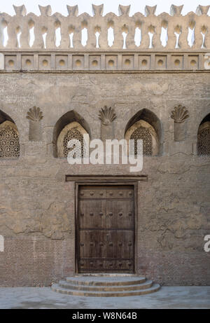 Invecchiato in legno porta a spiovente, arcuata forata finestra di stucco decorato con motivi floreali e tre passaggi su pietra muro in mattoni, Ibn Tulun Mosque, Ca Foto Stock