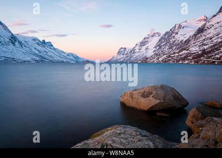 Ersfjord al tramonto in inverno con montagne innevate e le rocce in primo piano, Norvegia Foto Stock