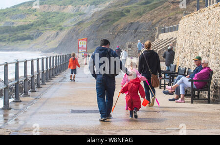 Charmouth, Dorset, Regno Unito. Il 10 agosto 2019. Meteo REGNO UNITO: vacanzieri avventurarvi in un blustery giornata al villaggio sul mare di Charmouth come unseasonably strong a sud-ovest si snoda continuano ad impasto lungo la costa sud occidentale il sabato pomeriggio. Warmings giallo per il vento ad alta velocità sono stati rilasciati attraverso il Sud Ovest. Credito: Celia McMahon/Alamy Live News. Foto Stock