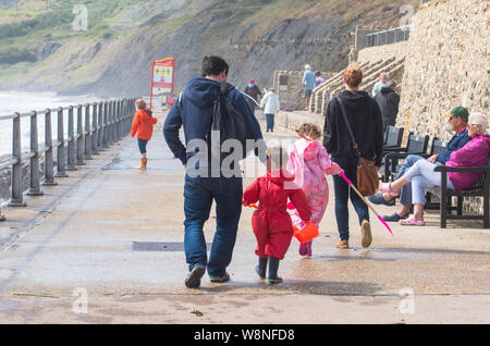 Charmouth, Dorset, Regno Unito. Il 10 agosto 2019. Meteo REGNO UNITO: vacanzieri avventurarvi in un blustery giornata al villaggio sul mare di Charmouth come unseasonably strong a sud-ovest si snoda continuano ad impasto lungo la costa sud occidentale il sabato pomeriggio. Warmings giallo per il vento ad alta velocità sono stati rilasciati attraverso il Sud Ovest. Credito: Celia McMahon/Alamy Live News. Foto Stock