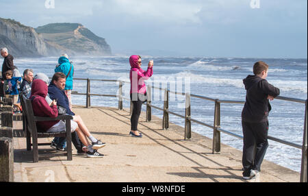 Charmouth, Dorset, Regno Unito. Il 10 agosto 2019. Meteo REGNO UNITO: vacanzieri avventurarvi in un blustery giornata al villaggio sul mare di Charmouth come unseasonably strong a sud-ovest si snoda continuano ad impasto lungo la costa sud occidentale il sabato pomeriggio. Warmings giallo per il vento ad alta velocità sono stati rilasciati attraverso il Sud Ovest. Credito: Celia McMahon/Alamy Live News. Foto Stock