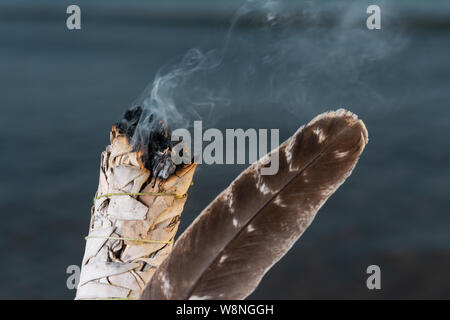 Sbavatura rituale utilizzando la masterizzazione spessa bundle frondoso di salvia bianco Grado A bloccate la Turchia sbavature giù sulla spiaggia al sorgere del sole di fronte al lago. Foto Stock