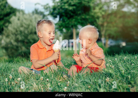 Due caucasica bambini divertenti ragazzi fratelli seduti insieme la condivisione di mangiare un gelato. Il Toddler più giovane pianto del bambino e il fratello più anziano teasing lui. L Foto Stock