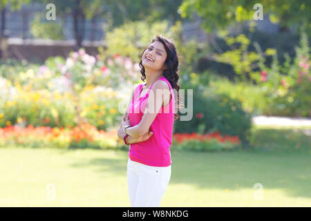 Giovane donna in piedi con le braccia incrociate in un giardino Foto Stock