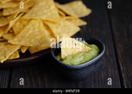 Popolari piatto messicano, nachos fatta con il mais tortilla chips o totopos e salsa guacamole su sfondo di legno. Foto Stock