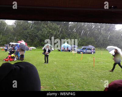 Evento annuale piovuto off - una solitaria figura si rifiuta di essere dissuaso dal guardare un evento in un festival come tutti gli altri curiosi rush per riparo da un acquazzone torrenziale Foto Stock