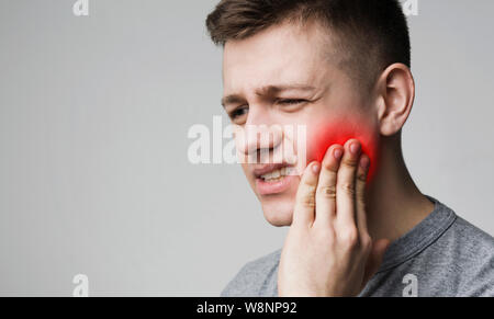 Frustrati giovane toccando il suo dente e faccia triste Foto Stock