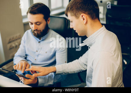 Due bello colleghi maschi interagenti con tablet schermo mentre seduti a tavola ufficio insieme e il lavoro.La navigazione uomini tablet in ufficio Foto Stock