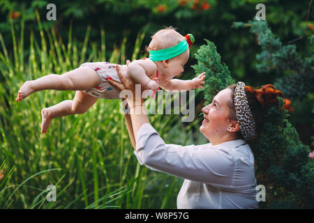 Felice famiglia armoniosa all'esterno. madre getta baby fino, ridendo e giocando in estate sulla natura. Foto Stock