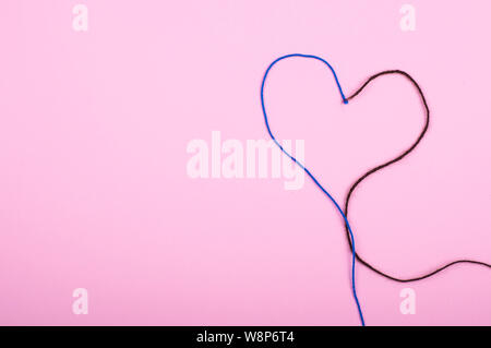 Filo di lana a forma di cuore su sfondo rosa. Due colori concept Foto Stock