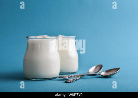 Lo yogurt greco in vasi di vetro con cucchiai su sfondo blu closeup Foto Stock