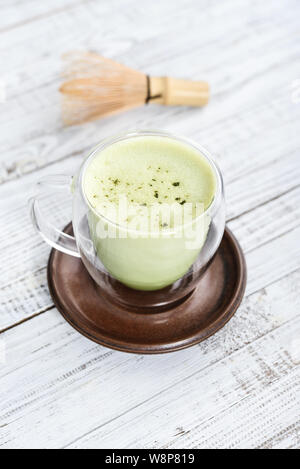 Tè verde Matcha latte con matcha in polvere e mescolare con una frusta di bambù su sfondo di legno closeup Foto Stock