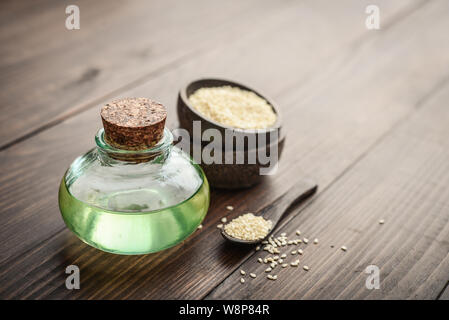 Olio di sesamo in una bottiglia di vetro e i semi su sfondo di legno Foto Stock