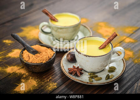 Tradizionale bevanda indiana curcuma latte è latte dorato con cannella, chiodi di garofano e pepe e curcuma su uno sfondo di legno con spezie Foto Stock