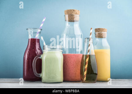 Arancione, verde e colorato di rosso frullati e succhi di frutta in vasetti di vetro su uno sfondo blu. Foto Stock