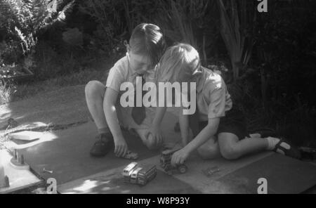 Degli anni Cinquanta, storico, due giovani ragazzi in camicie e cravatte giocare insieme con il loro giocattolo di metallo autobus al di fuori su di un piccolo giardino con patio, Inghilterra, Regno Unito. Foto Stock