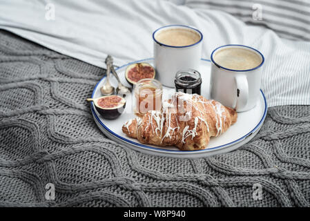 Vassoio con due tazze di caffè, diverse marmellate in vasetti e croissant  sul letto al momento della colazione Foto stock - Alamy
