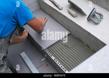Installatore mani lavorando su un nuovo ingresso di casa, locali e professionisti tuttofare applicando le piastrelle per le fasi. Foto Stock