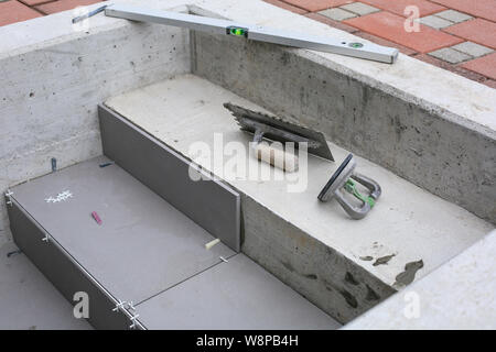 Installatore mani lavorando su un nuovo ingresso di casa, locali e professionisti tuttofare applicando le piastrelle per le fasi. Foto Stock