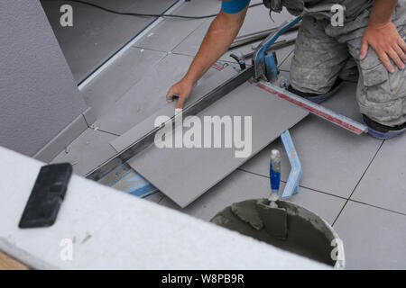 Installatore mani lavorando su un nuovo ingresso di casa, locali e professionisti tuttofare applicando le piastrelle per le fasi. Foto Stock