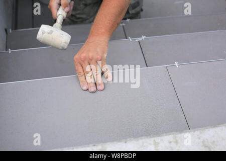 Installatore mani lavorando su un nuovo ingresso di casa, locali e professionisti tuttofare applicando le piastrelle per le fasi. Foto Stock