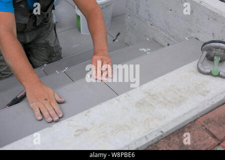 Installatore mani lavorando su un nuovo ingresso di casa, locali e professionisti tuttofare applicando le piastrelle per le fasi. Foto Stock