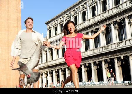 Matura in amore avente giocoso divertimento in viaggio Venezia holding hands in esecuzione a ridere a Venezia in Piazza San Marco. Felice una giovane coppia in vacanza di viaggio su Piazza San Marco. Felice l'uomo e la donna. Foto Stock