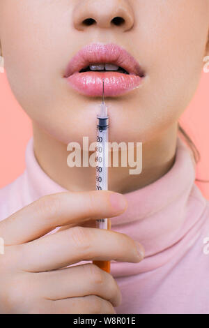 Closeup crop giovane donna in camicetta mostrando l'iniezione del farmaco nei pressi di labbra Foto Stock
