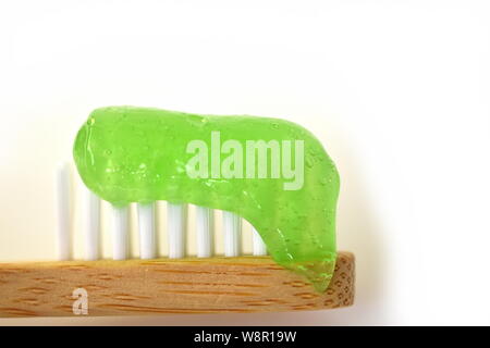 Primo piano della naturale, vegan , eco-friendly, socialmente responsabile, spazzolino da denti di legno con verde trasparente dentifricio in gel luminoso su sfondo grigio Foto Stock