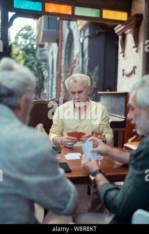 Grigio-dai capelli uomo barbuto giocando a carte con gli amici Foto Stock