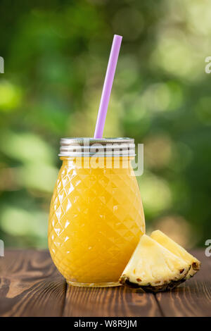 Ananas fresco succo in un barattolo di vetro sul tavolo in legno all'esterno. Estate bevanda rinfrescante Foto Stock