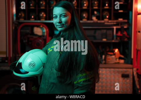 Foto di donna pompiere con capelli lunghi con casco nelle sue mani presso la stazione dei vigili del fuoco. Foto Stock