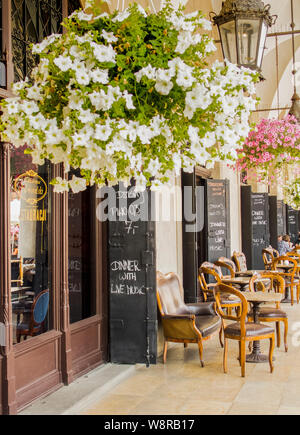 Cracovia, Poland-June 10,2015: coffee shop sotto i portici del panno hall di Cracovia con sedie di legno e appendere dei POT del fiore Foto Stock